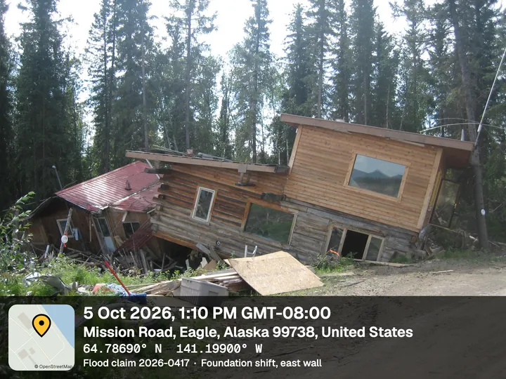 Flood-damaged log house tilted off its foundation, with the Bold stamp: date and time, Mission Road, Eagle, Alaska, Flood claim 2026-0417
