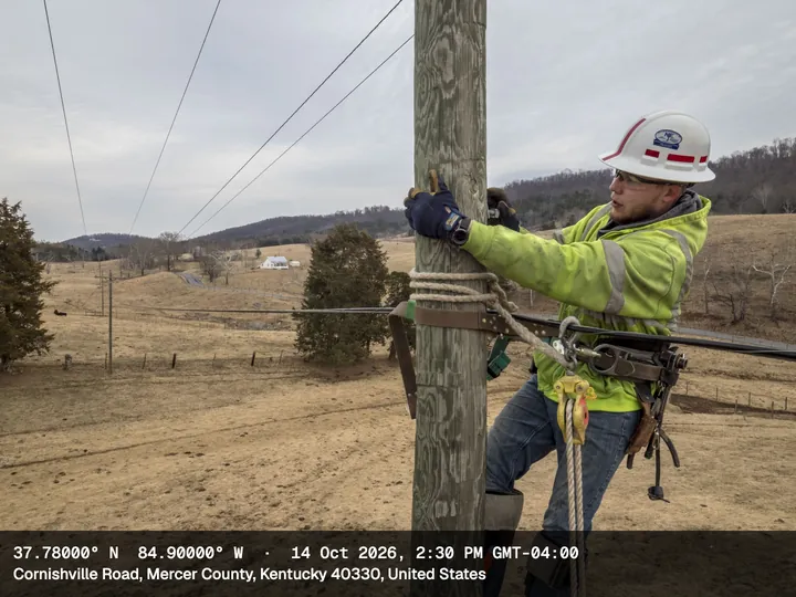 Lineman climbing a wooden utility pole in farmland, with the Compact stamp: coordinates, date and time, Cornishville Road, Mercer County, Kentucky